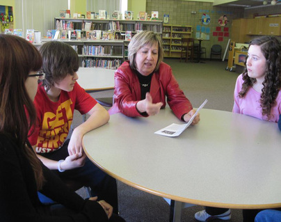 Female adult principal talking to Grade 8 students in library